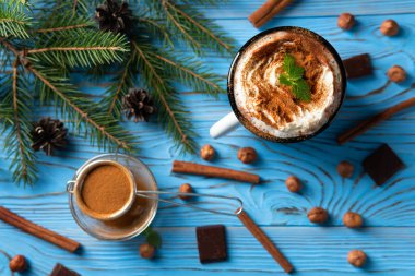 Kupa sıcak çikolata ve çırpılmış krema ile tarçın ile dekore edilmiş ve nane yaprakları üzerinde mavi bir ahşap masa