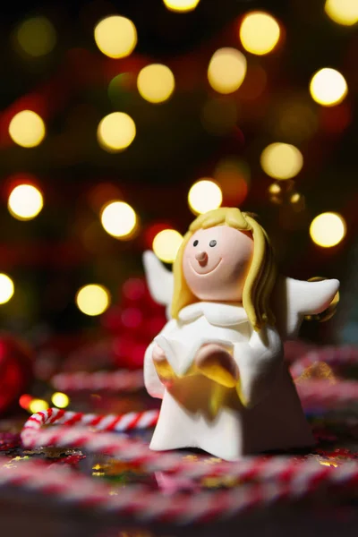 Closeup of toy angel figurine in glowing garland lights with striped string and glitters near
