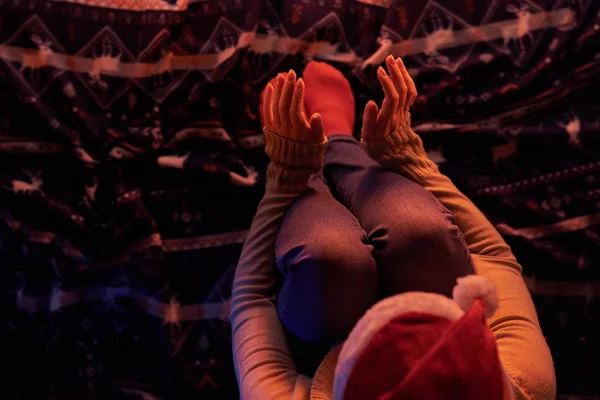 从上面的妇女在圣诞老人的帽子坐在格子在壁炉和温暖的光 — 图库照片