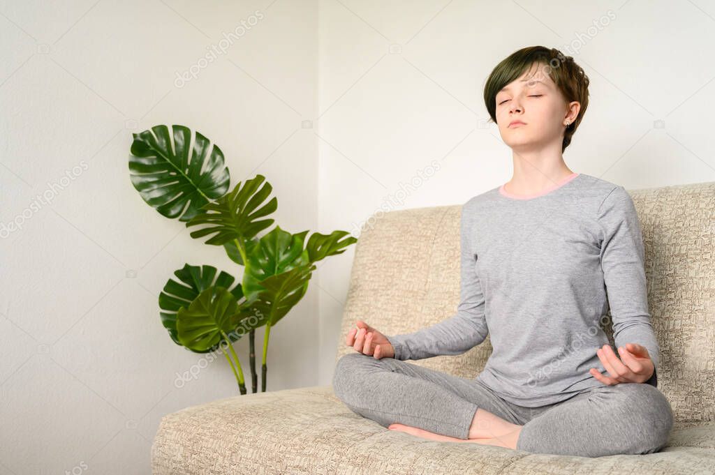 Teen girl meditate sitting in lotus position on the couch. Yoga at home.