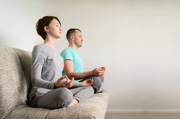 Father and daughter are meditating, sitting in lotus position on the couch. Yoga at home.