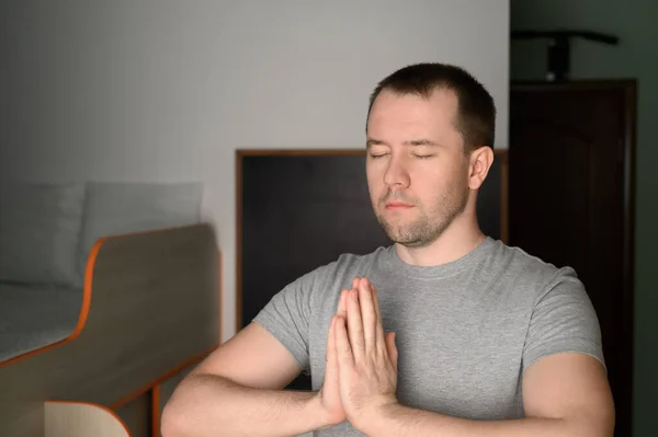 Young adult man stands in a tree pose while doing yoga at home.