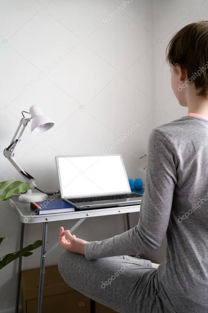 Teen girl is training at home, doing yoga exercises, sitting in lotus position, meditation.