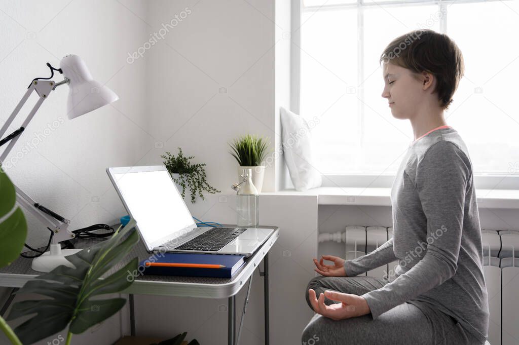 Teen girl is training at home, doing yoga exercises, sitting in lotus position, meditation.