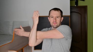 Genç bir adam evde egzersiz yaparken esneme hareketleri yapıyor..