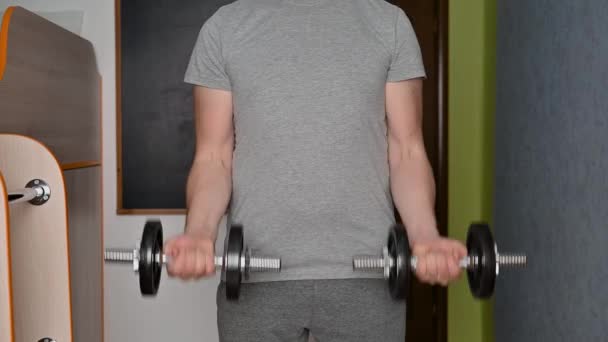 Young adult man lifts dumbbells in the room. — Stock Video