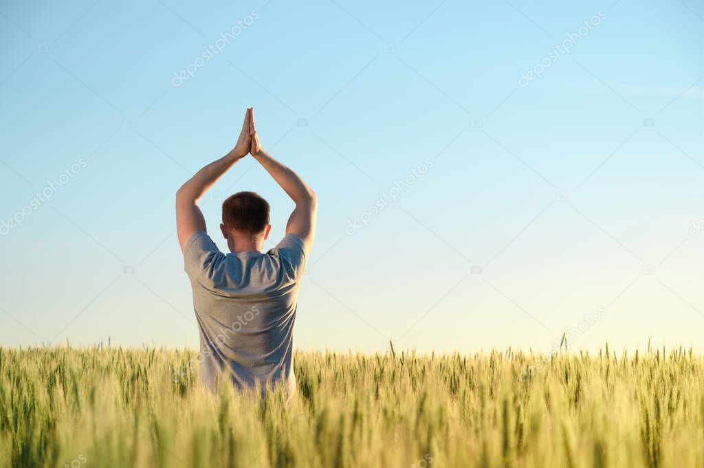 A man stands on a field in tall grass doing yoga during dawn.