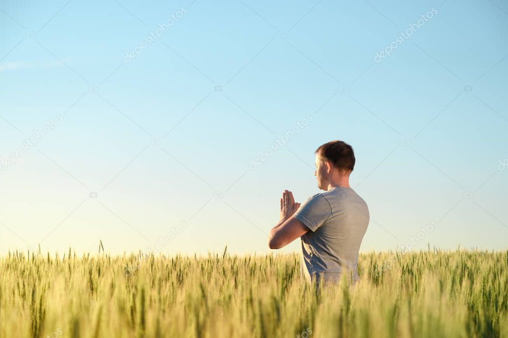 A man stands on a field in tall grass doing yoga during dawn.
