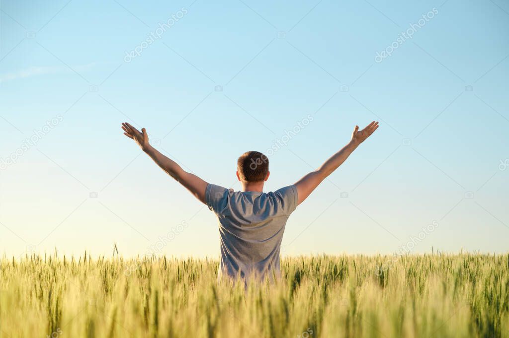 An adult man stands on a field in tall grass, arms spread out to the sides during dawn.
