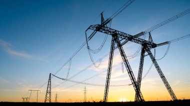 Gün batımında yüksek voltajlı sütunların siluetleri.