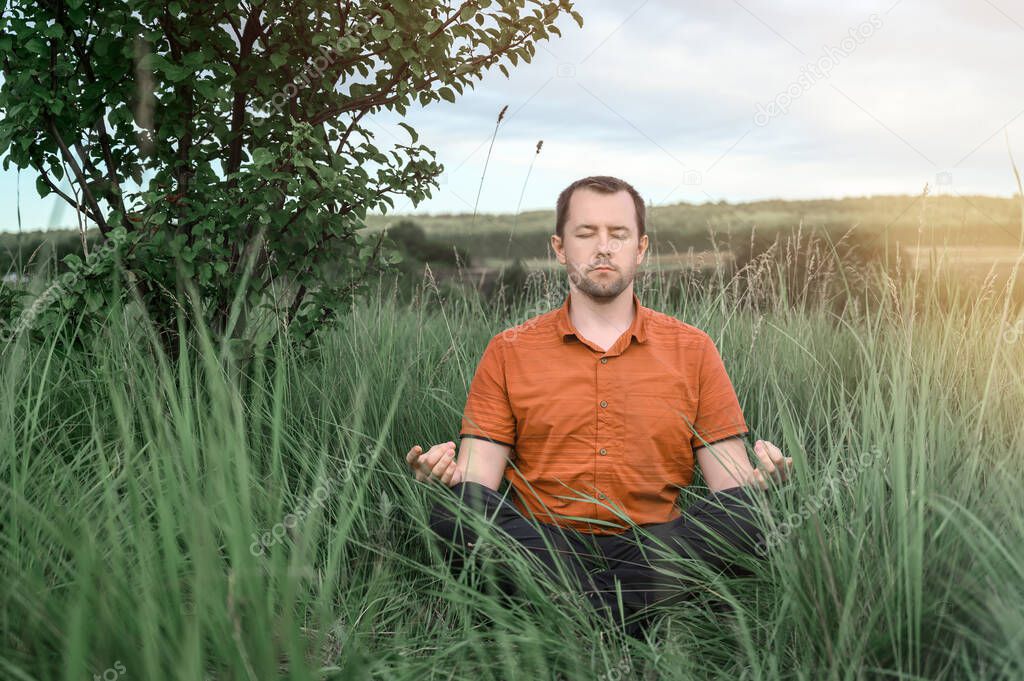 Adult man sitting in the Lotus position and meditating in tall grass. Concept digital detox, connection with nature.