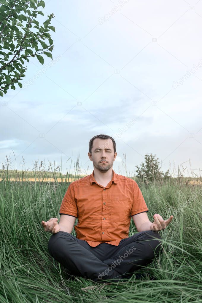 Adult man sitting in the Lotus position and meditating in tall grass. Concept digital detox, connection with nature.