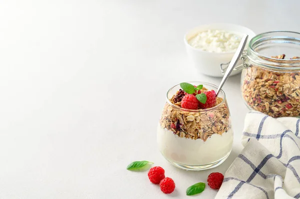 Parfait jogurt s granolou a malinami ve sklenici, světlé pozadí, kopírovací prostor. — Stock fotografie
