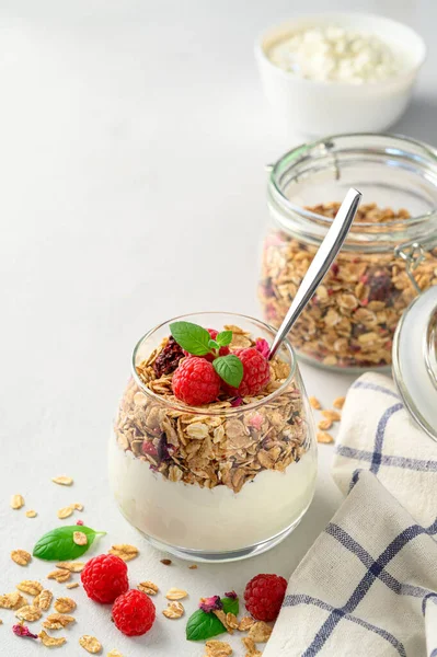 Yogurt parfait con muesli e lamponi in un bicchiere, sfondo chiaro, spazio per la copia. — Foto Stock