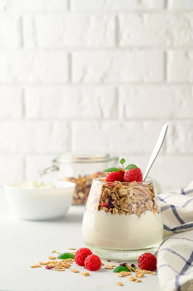 Yogurt parfait con muesli e lamponi in un bicchiere, sfondo chiaro, spazio per la copia. — Foto Stock