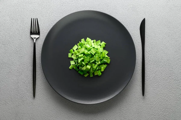 Zöldhagymát szeletelt egy fekete tányérba késsel és villával. Allium diutans hagyma. — Stock Fotó