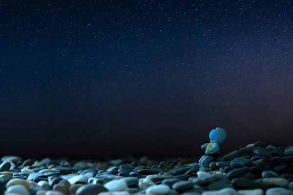 Viaje al concepto de otros planetas. La figura del astronauta se sienta sobre las piedras sobre el fondo del cielo estrellado. — Foto de Stock