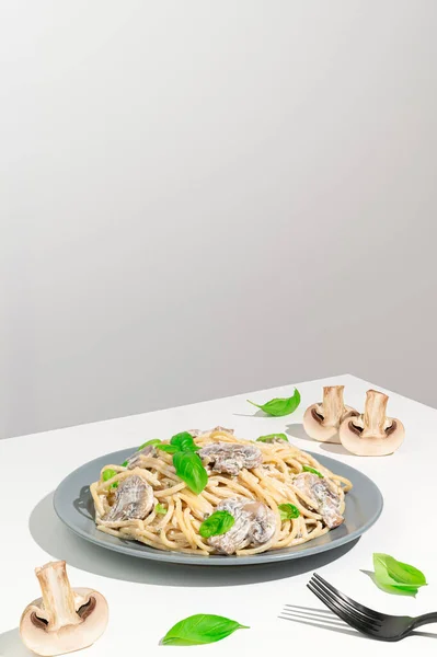 Spaghetti med krämig sås, svamp, grön basilika på ett vitt bord. Vegetarisk italiensk pasta med champinjoner i en grå platta. — Stockfoto