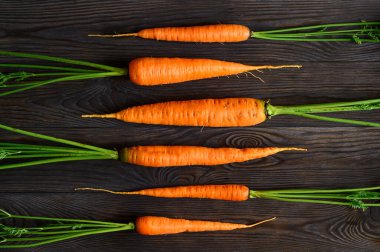 Koyu ahşap zemin üzerinde yeşil tepeli çiğ havuç deseni. Çevre yiyecekleri, köy tarzı..