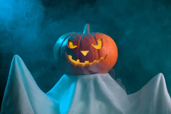 Ett spöke med ett läskigt huvud glödande jack-o-lantern pumpa står i dimman i skymningen. — Stockfoto