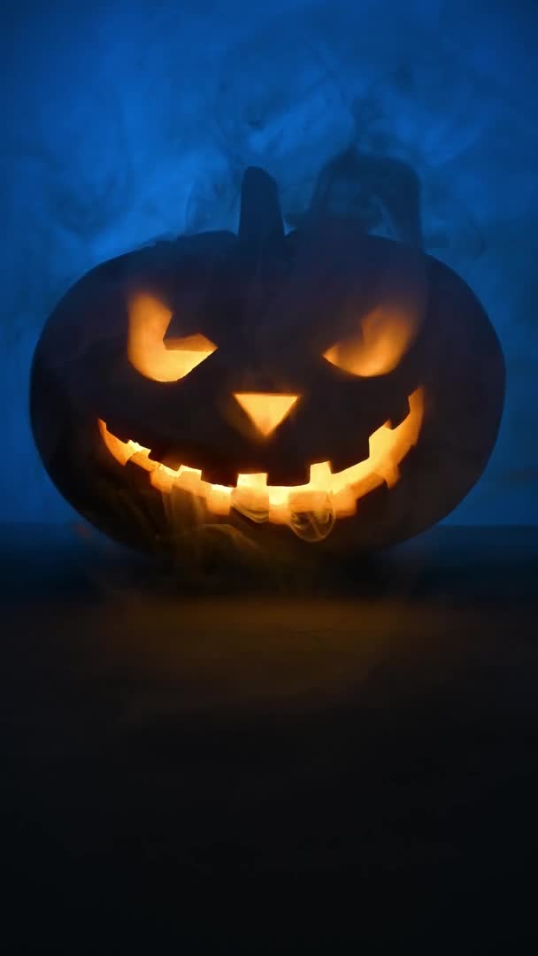 Skrämmande glödande ansikte Halloween pumpa i blå rök. — Stockvideo