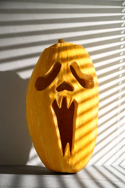 Fondo de vacaciones de Halloween. Espeluznante calabaza de Halloween en la mesa, iluminada por la luz del sol a través de las persianas. — Foto de Stock