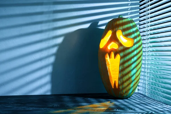 Halloween holiday background. Spooky Halloween pumpkin on the table, illuminated by moonlight through the jalousie. — Stock Photo, Image