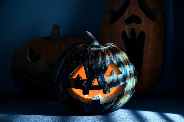 Halloween vakantie achtergrond. Drie Spooky Halloween pompoenen op de tafel, verlicht door maanlicht door de jaloezie. — Stockfoto