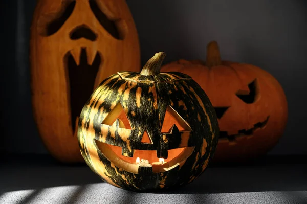 Halloween semester bakgrund. Tre läskiga halloween pumpor på bordet, upplysta av solljus genom jalousie. — Stockfoto