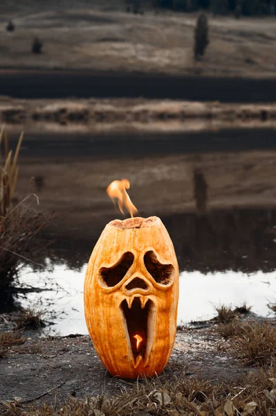 Concepto de horror de Halloween. Calabaza de Halloween se quema en la orilla del estanque. — Foto de Stock