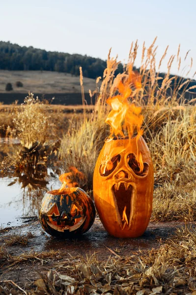 Duas abóboras de Halloween estão queimando na margem do lago. — Fotografia de Stock