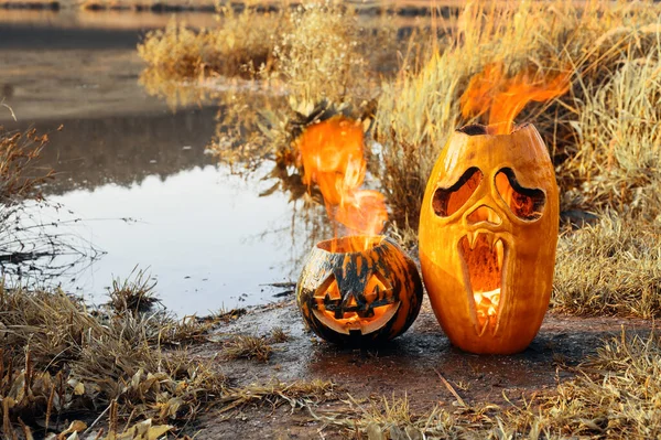 Duas abóboras de Halloween estão queimando na margem do lago. — Fotografia de Stock