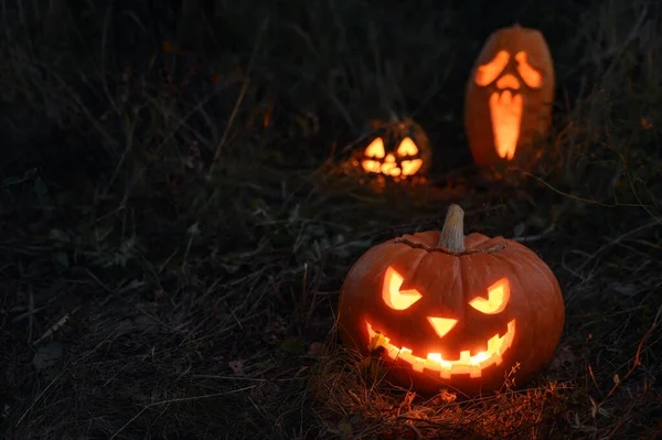 Drie gloeiende spookachtige Halloween pompoen op de grond 's nachts. — Stockfoto