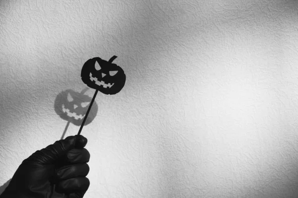 Halloween Decoration. Black paper Halloween pumpkin on a stick in hand against a white wall background. — Stock Photo, Image