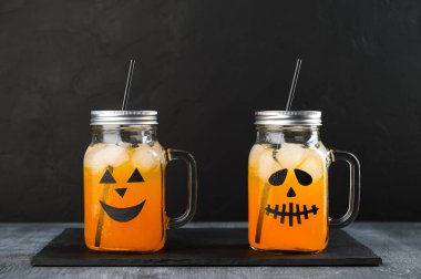 Cadılar Bayramı balkabağı siyah arka planda korkunç yüzlerle süslenmiş cam kavanozlarda moktail..