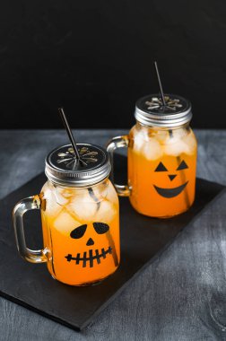 Cadılar Bayramı balkabağı siyah arka planda korkunç yüzlerle süslenmiş cam kavanozlarda moktail..