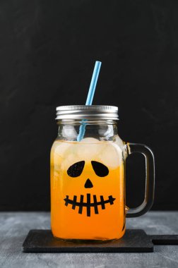 Cadılar Bayramı balkabağı siyah arka planda korkunç bir yüzle süslenmiş cam kavanozda moktail..