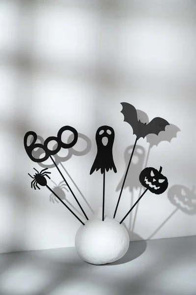 Halloween home decorations. Painted white pumpkin and black Halloween frightening puppets on sticks on a light gray background. — Stock Photo, Image
