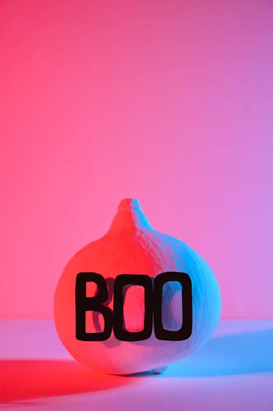 Halloween home decorations. A painted white pumpkin with the word Boo, illuminated with neon light. — Stock Photo, Image