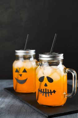 Cadılar Bayramı balkabağı siyah arka planda korkunç yüzlerle süslenmiş cam kavanozlarda moktail..