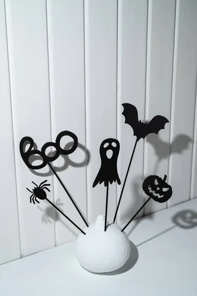 Halloween home decorations. Painted white pumpkin and black Halloween scary shadow puppets on sticks against a white wooden wall. — Stock Photo, Image