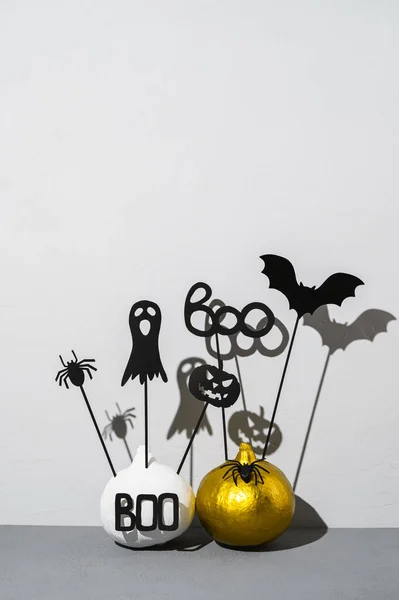 Halloween home decorations. Painted white and gold pumpkins with scary black Halloween objects with shadows on a gray background.