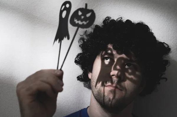 Porträt eines erwachsenen Mannes in schwarzer Perücke mit Schatten von Halloween-Kürbis und einem Geist auf seinen Augen. — Stockfoto