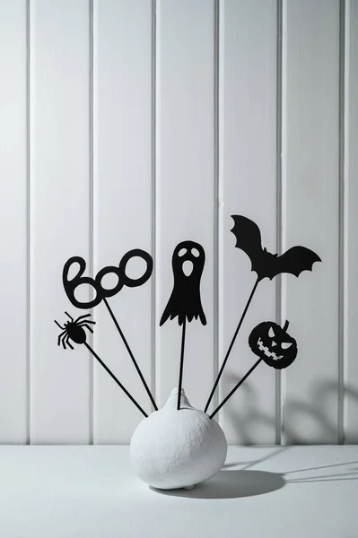 Halloween home decorations. Painted white pumpkin and black Halloween scary shadow puppets on sticks against a white wooden wall. — Stock Photo, Image