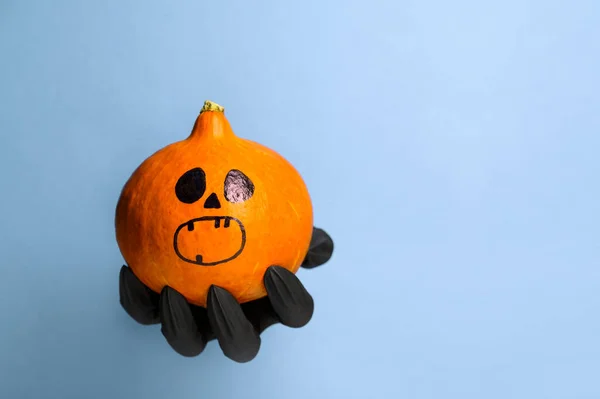 Creepy Black Hand holds a Halloween pumpkin on a pastel blue background. Halloween symbol. — Stock Photo, Image