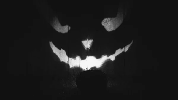 Halloween-Kürbis erleuchtet nachts draußen eine Holzwand. Glühender Jack-O-Lantern-Kürbis an der Wand. Schwarz-Weiß-Fotografie. — Stockfoto