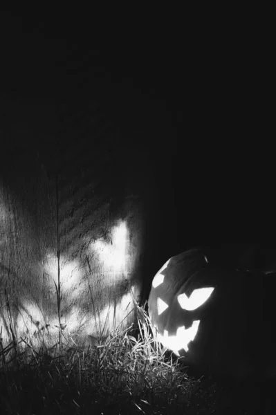 Halloween pumpkin lights up a wooden wall at night outside. Glowing face Jack-O-Lantern pumpkin on the wall. Black and white photography. — Stock Photo, Image
