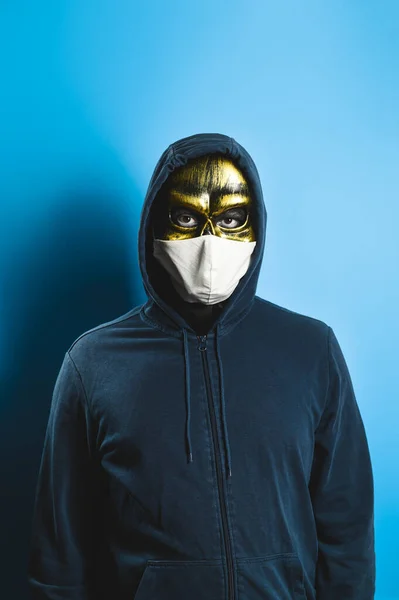 Era Covid. Novo conceito normal. Retrato de um homem com uma máscara de crânio e uma máscara médica protetora sobre um fundo azul. Halloween festa traje. — Fotografia de Stock