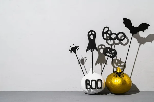 Halloween home decorations. Painted white and gold pumpkins with scary black Halloween objects with shadows on a gray background.