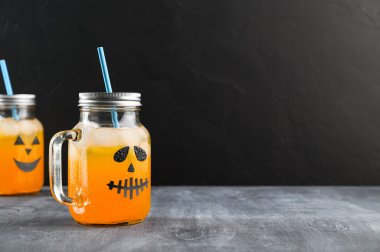 Cadılar Bayramı balkabağı, cam kavanozlarda siyah arka planda, tahtada korkunç yüzler olan kokteyller..